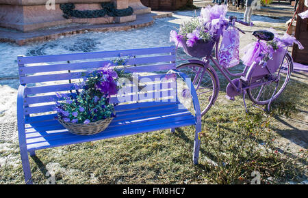 Banc en bois et de vieux vélo peint en violet et décoré avec des fleurs et des accessoires assortis. Banque D'Images