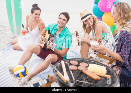 Groupe d'amis avec des boissons et de la guitare assis près d'un barbecue Banque D'Images