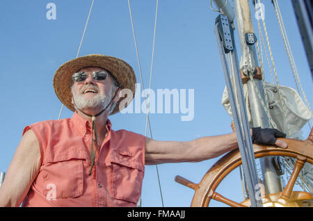 Un homme à la barre de son ketch classique jouit de la journée d'été sous un ciel bleu. Banque D'Images