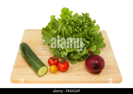 Ingrédients de la salade, Laitue, Concombres, tomates et un oignon rouge sur une planche à découper en bois blanc isolé contre Banque D'Images