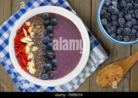 Frappé aux bleuets bol avec les amandes, les baies de goji et chia seeds sur une table en bois avec des bleuets frais Banque D'Images