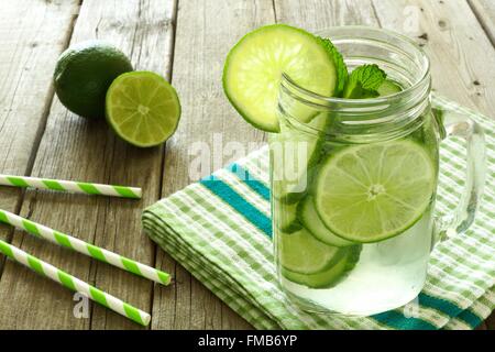 L'eau de désintoxication avec de la chaux et concombres dans un pot Mason sur une table en bois avec un tissu à carreaux et des pailles. Banque D'Images