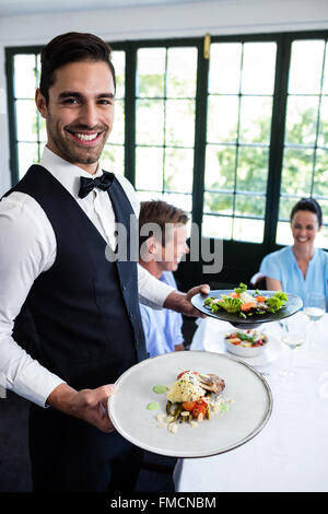 Portrait of waiter standing avec repas à côté de clients Banque D'Images