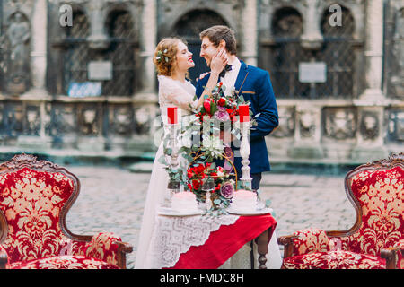 Charmante blonde bride coups doucement son visage souriant et marié. Vintage table avec des bougies et des fleurs à l'avant-plan Banque D'Images