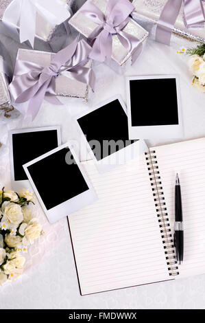 Album de mariage et stylo à bille avec impressions photo vierge mis sur la dentelle mariée avec plusieurs cadeaux de mariage d'argent et rose bouquets. Banque D'Images