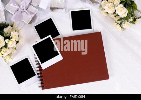 Album photo rouge blanc avec des impressions photo instantanée sur dentelle mariée avec plusieurs cadeaux de mariage d'argent et rose blanche bouquets. Banque D'Images