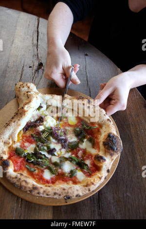 Une femme coupe une pizza style napolitain avec des ciseaux. Banque D'Images