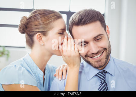Happy businesswoman whispering pour collègue masculin Banque D'Images