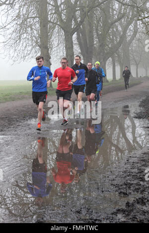 Nonsuch Park, Cheam, Surrey, UK. 12 mars 2016. C'était un début de journée brumeuse au Nonsuch Park, Cheam, Surrey, UK, où près de 450 coureurs ont pris part à l'hebdomadaire 5k parkrun. L'événement est libre d'entrer et est pour les coureurs de toutes les normes. Ici un groupe dodge les flaques boueuses comme ils course pour un bon moment. Banque D'Images