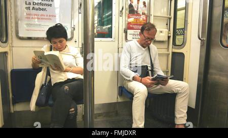 Deux passagers d'un train de métro de Paris, on lit un magazine, l'autre un livre. Banque D'Images