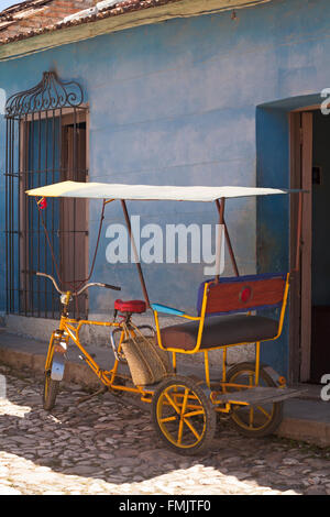 La vie quotidienne à Cuba - vélos taxis colorés en stationnement sur rue pavée à l'extérieur de bâtiment bleu à Trinidad, Cuba en Mars Banque D'Images