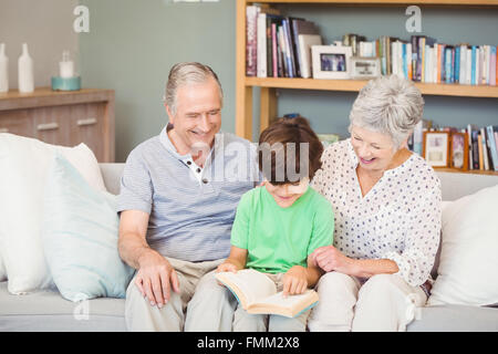 Aider les grands-parents petit-fils lors de la lecture de livre dans la salle de séjour Banque D'Images