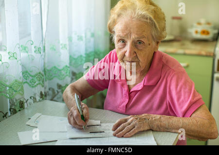 Une vieille femme assise à la table remplit le projet de loi pour les services publics. Banque D'Images