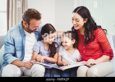 Les parents à la recherche de photo book alors qu'il était assis avec ses filles Banque D'Images