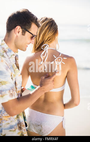 L'homme faisant un symbole de soleil sur womans retour lors de l'application d'une lotion écran solaire Banque D'Images
