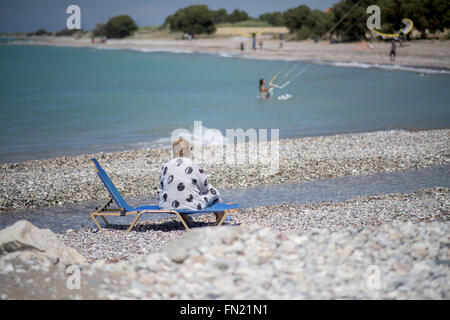 Une vieille femme assise sur une chaise longue sur une plage Banque D'Images