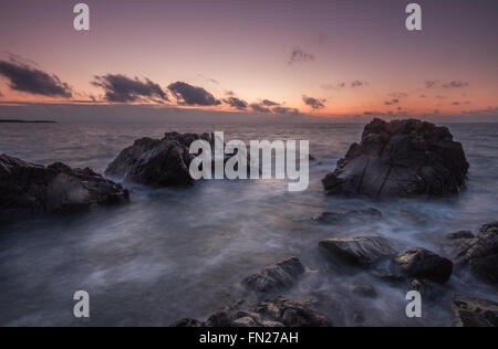 Un boîtier robuste, sunrise côtières à Cornwall avec des vagues circulant sur les rochers de granit. Une longue exposition de droit de l'océan au coucher du soleil Banque D'Images