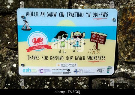 Merci de faire notre bilingue beach Smoke Free signe sur un mur au-dessus du petit havre de Pembrokeshire Coast National Park Plage Banque D'Images