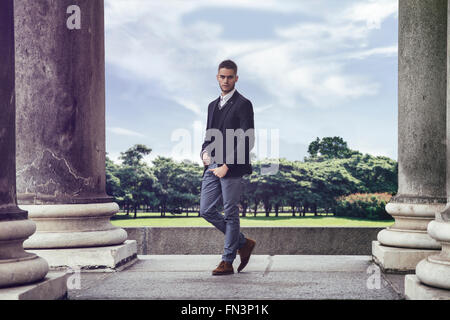 Portrait d'homme barbu élégant en costume élégant à la caméra à l'encontre de parc et bâtiments historiques Banque D'Images