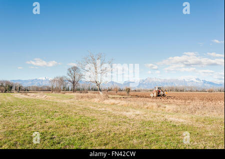 Paysage agricole. Avec le tracteur laboure un champ. Les montagnes en arrière-plan. Banque D'Images