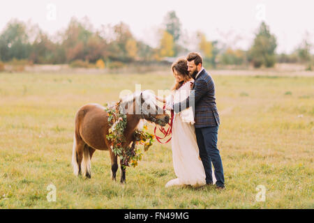 Lovely wedding couple caresser petit poney sur le terrain Banque D'Images