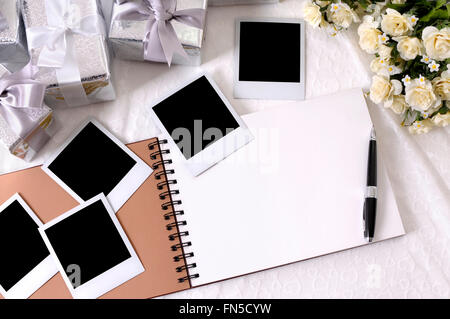 Album photo avec impressions photo instantanée vide posé sur la dentelle mariée avec plusieurs cadeaux de mariage d'argent et de roses blanches. Banque D'Images