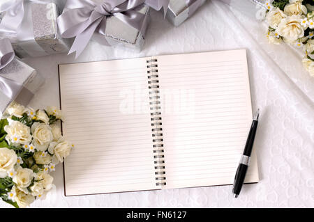 Arrière-plan de mariage avec carnet et un stylo posé sur la dentelle mariée avec plusieurs cadeaux de mariage d'argent et rose bouquet. Banque D'Images