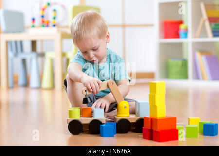 Enfant garçon assis sur le plancher et joue avec des blocs de construction et location Banque D'Images