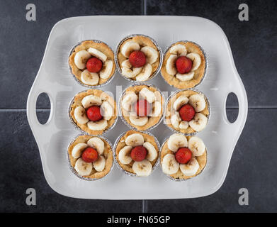 Tartelettes aux fraises et neuf avec des tranches de banane sur le plat blanc fond texturé et sombres. Vue d'en haut. Banque D'Images