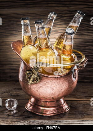 Bouteilles de bière froide dans le godet d'airain sur la table en bois. Banque D'Images