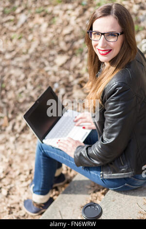 Jeune femme heureuse avec de longs cheveux à l'aide de l'ordinateur portable sur les escaliers dans le parc. Vue aérienne de droit Banque D'Images