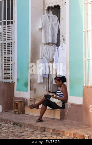 La vie quotidienne à Cuba Cuba - jeune femme s'assit sur le pas de la porte de la rue en faisant la couture de vêtements suspendu à Trinidad, Cuba en Mars Banque D'Images