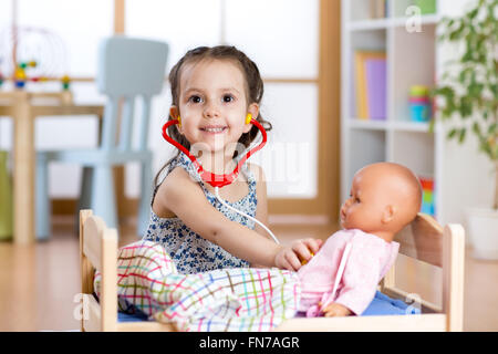 Enfant fille jouant le rôle médecin examinant sa poupée à l'aide de jeu de stéthoscope de jeux à la maison, à l'école ou au jardin d'enfants Banque D'Images