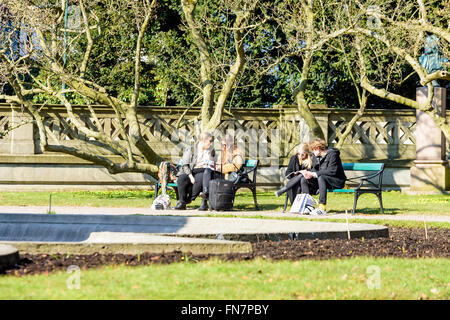 Lund, Suède - 12 mars 2016 : pas de jeunes personnes adultes assis sur banc de parc en regardant les brochures ou catalogues. L'uni Banque D'Images