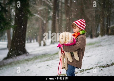 Boy carrying chiot golden retriever dog in snow Banque D'Images