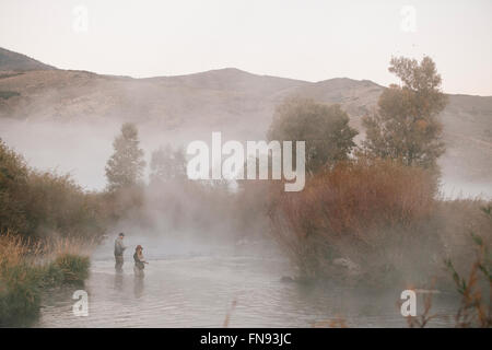 Un couple, un homme et femme debout au milieu de la pêche de mouche d'eau dans une rivière. Banque D'Images