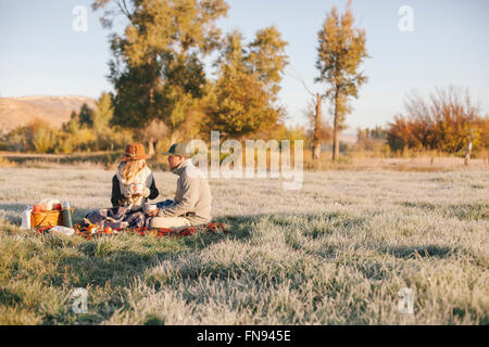 Un couple, un homme et une femme ayant un pique-nique d'hiver, assis sur un tapis en tartan. Banque D'Images