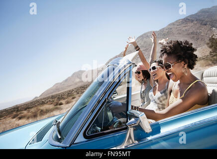Trois jeunes dans une voiture décapotable bleu pâle, la conduite sur route ouverte sur une plaine sèche, Banque D'Images