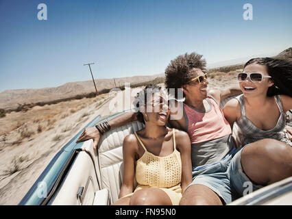 Trois jeunes dans une voiture décapotable bleu pâle, la conduite sur route ouverte sur une plaine sèche, Banque D'Images