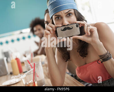 Une femme tenant une photo d'une moustache sur son smart phone juste sous son nez. Banque D'Images