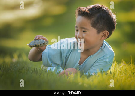 Un garçon couché sur l'herbe, tenant un petit restaurant terrapin ou tortue. Banque D'Images