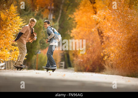 Deux garçons sur skate boards sur une route dans les bois aux couleurs de l'automne feuillage. Banque D'Images