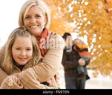Une famille, mère, fille, père et fils, sous un auvent de feuilles d'automne sur les arbres. Banque D'Images