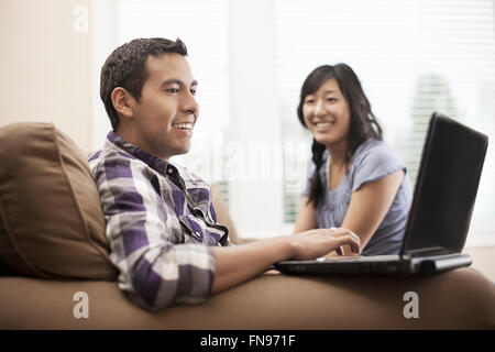 Un couple assis sur un canapé, un homme à l'aide d'un ordinateur portable. Banque D'Images
