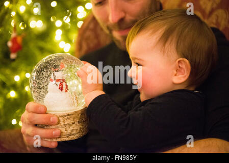 Une famille à la maison le jour de Noël. Un père et sa petite fille regardant un snowglobe. Banque D'Images