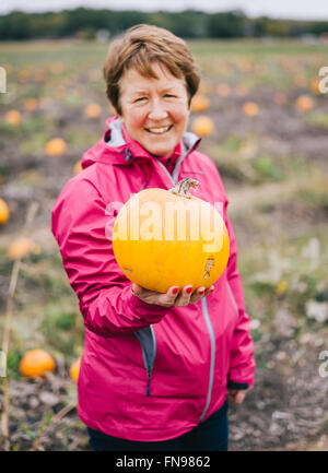 A young woman in a Red Jacket, tendent un grand orange citrouille. Banque D'Images
