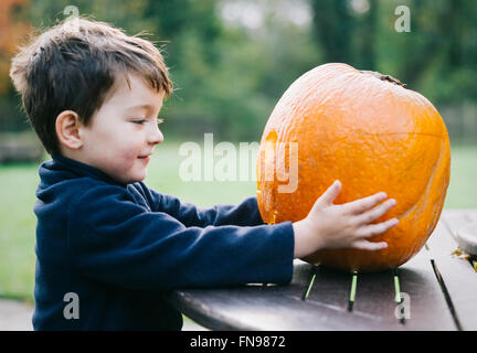 Un petit garçon tenant une grande peau d'orange citrouille. Banque D'Images