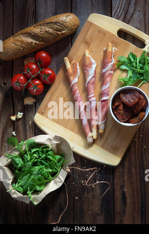 Bâtonnets enveloppés dans du jambon de Parme avec des tomates, roquette et du pain Banque D'Images