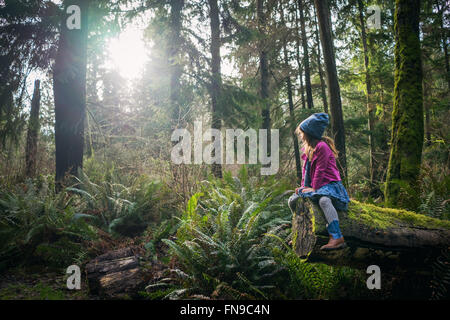 Jeune fille assise sur l'arbre couvert de mousse dans la forêt Banque D'Images