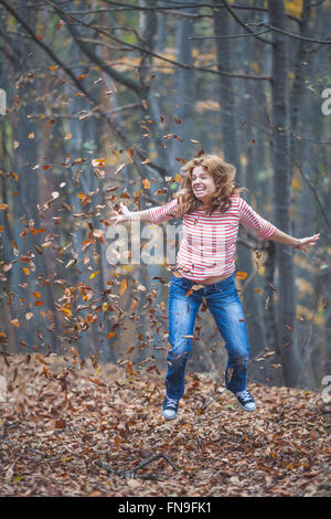 Femme du saut et du lancer les feuilles d'automne dans l'air Banque D'Images